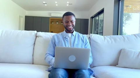Young african american man using laptop while sitting comfortably on a modern Stock Footage 348249409