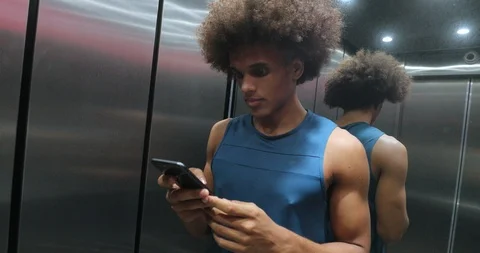 Young african black man checking cellphone device inside elevator, person ste Stockbeeldmateriaal 118637298