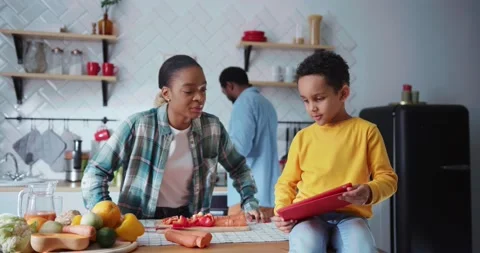 Young african boy helping his mom cooking dinner reading instructions on online Stock-Footage 146540682