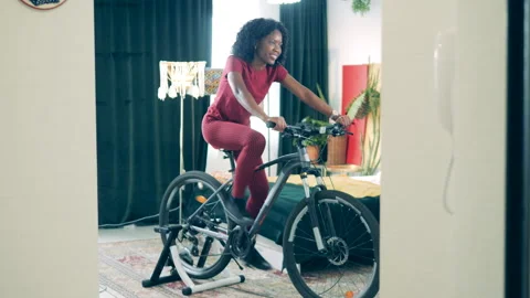 Young african lady is using a cycling machine to train at home Stock Footage 267528304