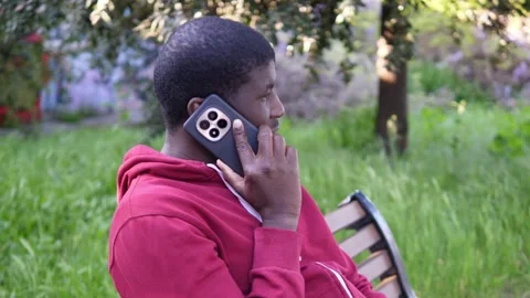 Young African man on bench talking on phone with friend side view Vidéo 332418428