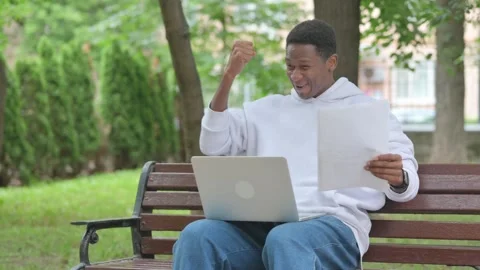 Young African Man Cheering while Working with Laptop and Documents Outdoors Stockbeeldmateriaal 311852119