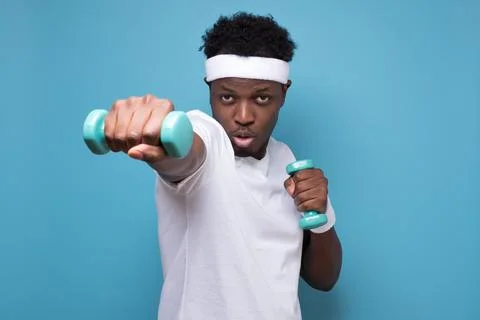 Young african man doing exercise with dumbbells spend time in gym. Stock Photos