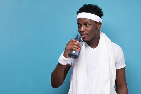 Young african man drinking cold water from plastic bottle after training at gym. Stock Photos