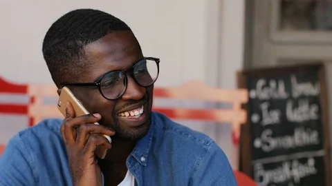 Young African man in glasses calling on mobile phone on terrace at dinner hour Stock Footage 81833085