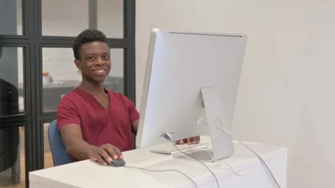 Young African Man Smiling at Camera while Working on Desktop Computer Stock Footage 303209986