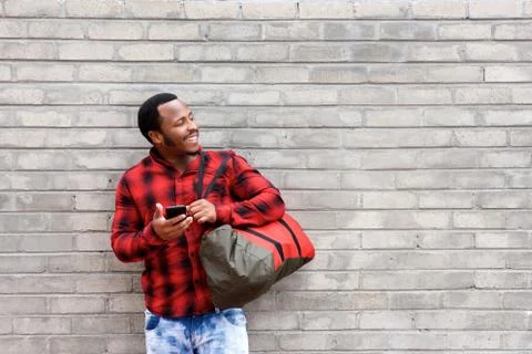 Young african man standing against wall with bag and cellphone Foto stock
