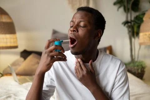 Young african man using asthma inhaler sitting at home Stock Photos