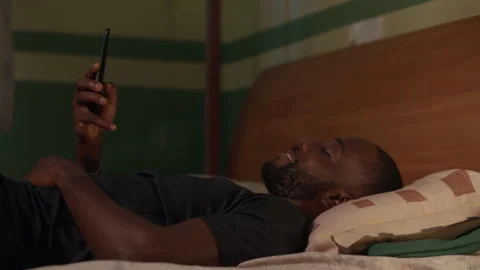 Young African man using his phone on his bed at night. 動画素材 345754639