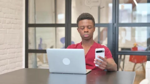 Young African Man Using Phone with Laptop Stock Footage 303211318