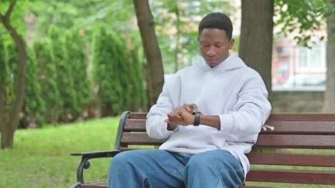 Young African Man Using Smart Watch on Park Bench Stockbeeldmateriaal 311850066