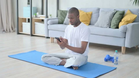 Young African Man using Smartphone on Yoga Mat at Home Video stock 154715350
