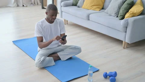 Young African Man using Smartphone on Yoga Mat at Home Video stock 154715638