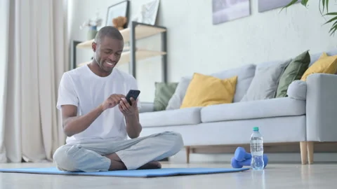 Young African Man using Smartphone on Yoga Mat at Home Stock Footage 154718030