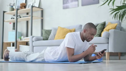 Young African Man using Smartphone Laying on Yoga Mat Stock Footage 154718689