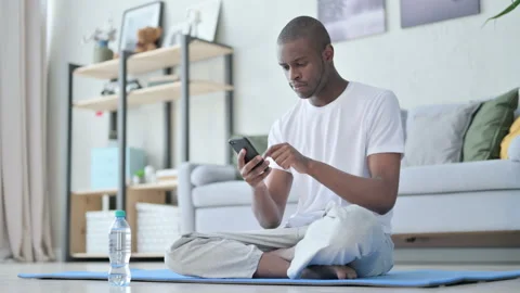 Young African Man using Smartphone on Yoga Mat at Home Stock Footage 154721254
