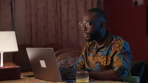 Young African man working on a laptop computer from home at night. Stock Footage 345756202