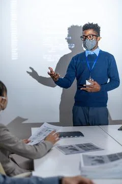 Young African programmer in protective mask standing by interactive screen Foto stock