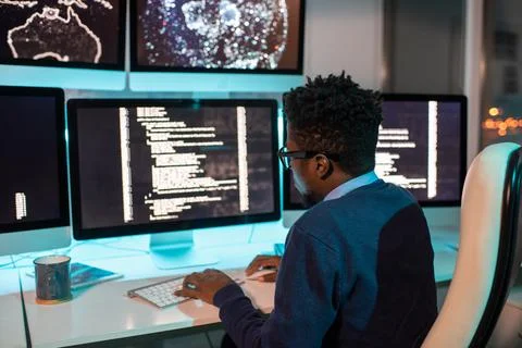 Young African software developer working late in front of computer screen with 写真素材