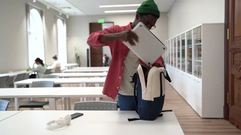 Young African student guy finished study putting laptop and textbook in backpack Stock Footage 226828447