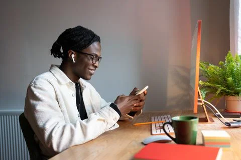 Young African student guy using smartphone, chatting with friends while studying Stock Photos