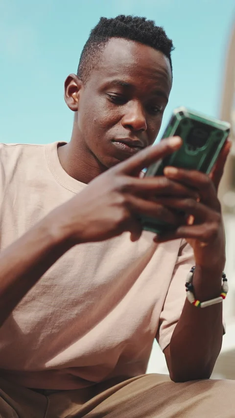 Young african student sits outside of university, uses cellphone, taps on Stock Footage 226935926