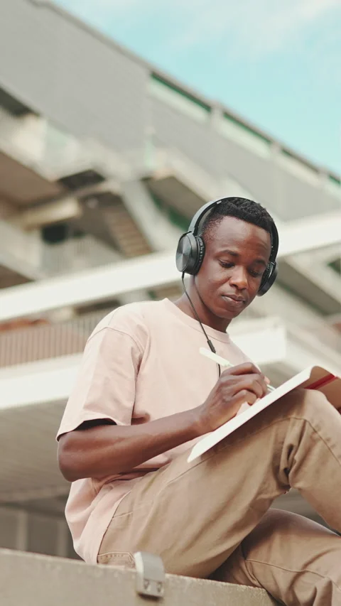 Young african student sitting outside of university and taking notes while study Stockbeeldmateriaal 226936346