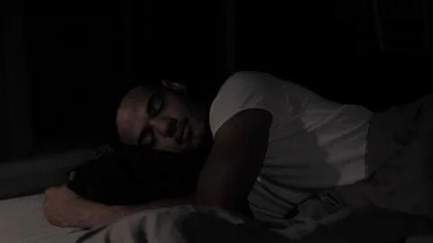 Young afro american man sleeping with pillow and moving at night in his bed in Video stock 110772236