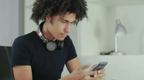 The young Afro-American sits on a sofa and watches news in phone Stock Footage 58587154
