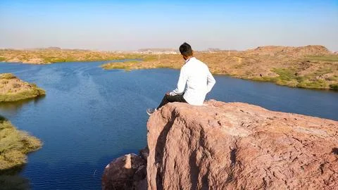 A young alone man sitting on the mountain and enjoying scenery view of lake Stock Photos