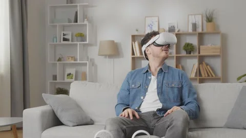 Young amazed man using his VR headset for watching the 360 video while sitting Stock Footage 169320715