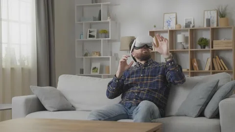 Young amazed man using his VR headset for watching 3D video while sitting on Stock Footage 169321221