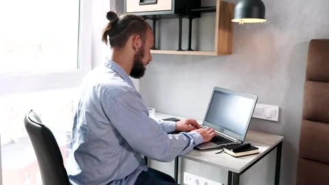 Young american guy sitting at a table, looking out the window and typing a me Stock Footage 136626102