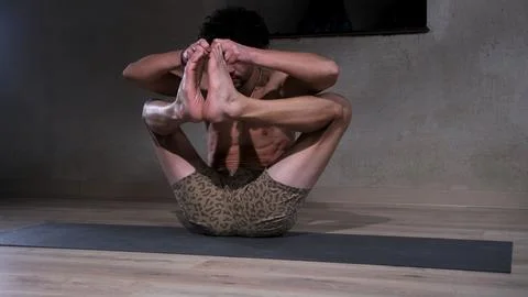 A young and athletic man does yoga and performs complex asanas Stock Photos