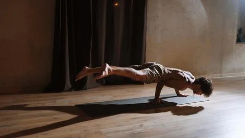 A young and athletic man does yoga and performs complex asanas Stock Photos