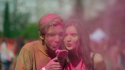 Young and cheerful guy and girl blowing paints into the camera at Holi festival Stock Footage 231125311