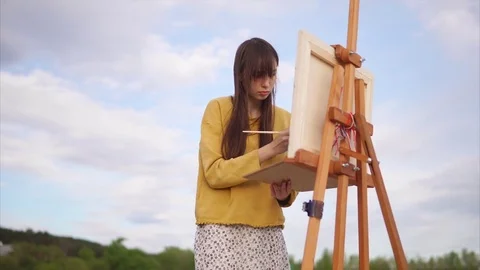 Young and creative artist paints a picture on canvas in an open air Stock Footage
