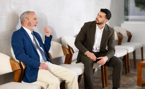Young and elderly men talking while waiting in job interview queue Stock Photos