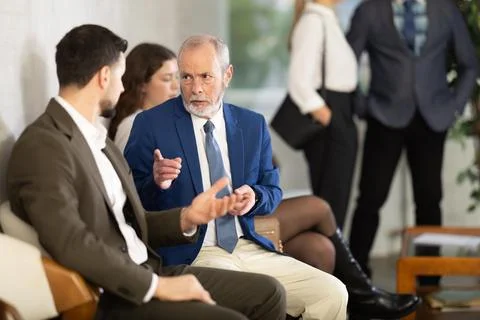 Young and elderly men talking while waiting in job interview queue Foto stock
