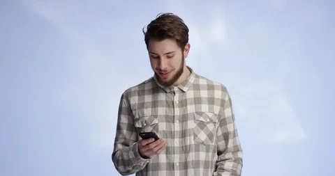 Young and good looking man typing on his phone and smiling into the camera af Stock-Footage 99414941