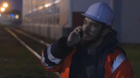 Young and happy worker in hard helmet talking by phone at night. 4k Video stock 83761111
