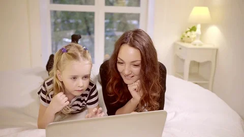 A young and pretty mother and her daughter watching movies on a laptop, a woman Stock Footage