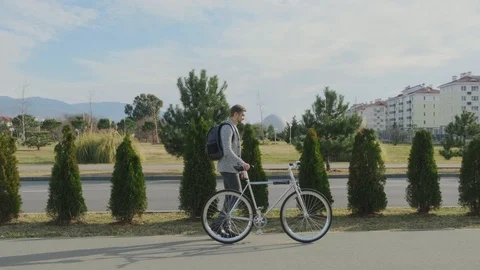A young and stylish man with a backpack is walking on the sidewalk with a Stock Footage 121883485