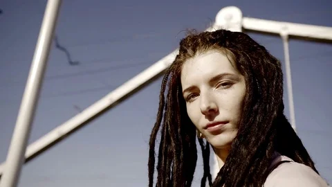 A young and stylish woman with dreadlocks walks against the backdrop of urban bu Stock Footage