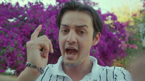 Young angry man making a video call on her smartphone near a flowering tree. Stock Footage 166160915