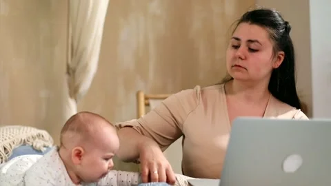 Young angry mother using laptop talking with baby girl crying on background. Onl 스톡 동영상 146307539
