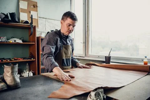 A young apprentice in a boot workshop prepares leather for further use on a Stock Photos
