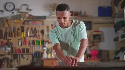 Young apprentice at carpenter workship sawing and measuring piece of wood w.. 库存照片