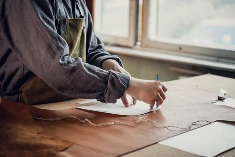 A young apprentice transfers a pattern from paper to leather using a pencil in Stock Photos