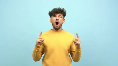 Young arab man pointing up, looking surprised and amazed, is presenting a Stock Footage 138665235